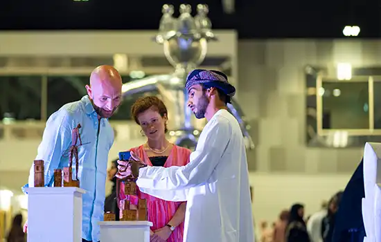Visitors observing and discussing art pieces at Muscat Art Exhibition 2024.