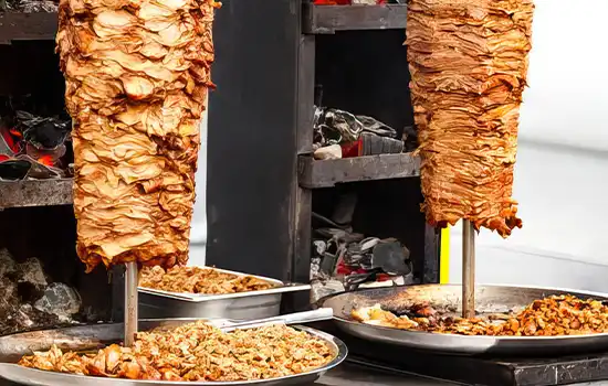 The History of Shawarma in the Gulf and Its Arrival in Oman 1 Image of shawarma on large rotating spits being cooked using traditional Middle Eastern methods.